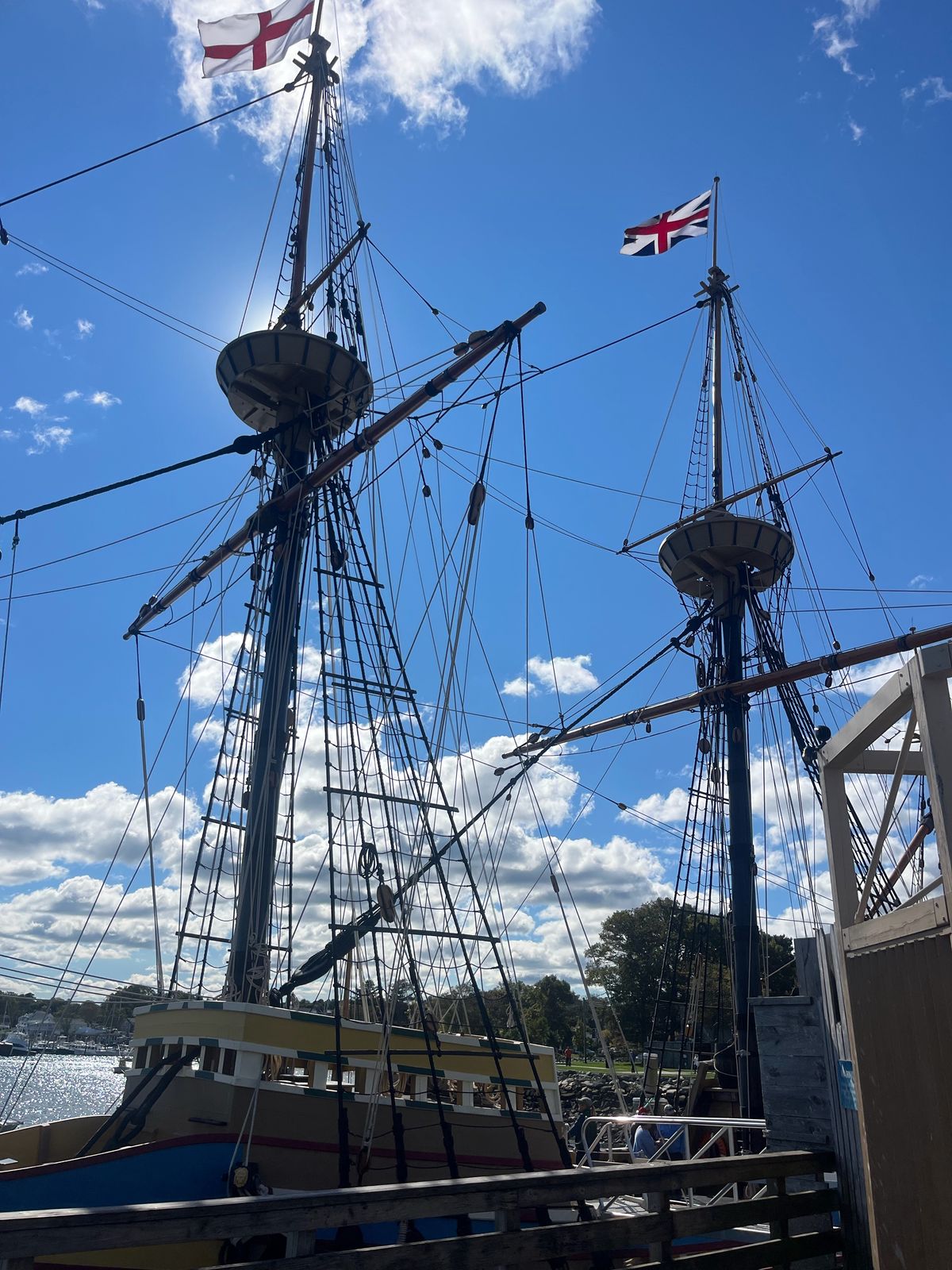 Tall ship masts and rigging flying English flags against a blue sky